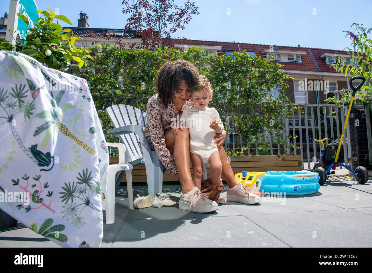 Ein freudiger Moment, als eine Mutter ihrem Kleinen hilft, ein paar Schritte in den sonnigen Hinterhof zu gehen. Stockfoto