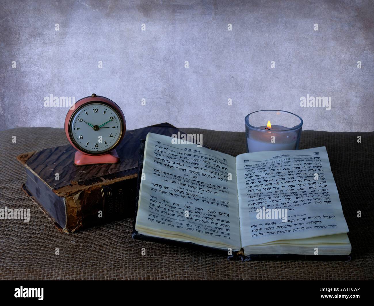 Zeitlose Ruhe mit einer Vintage-Uhr, flackernder Kerze und einem offenen Buch Stockfoto