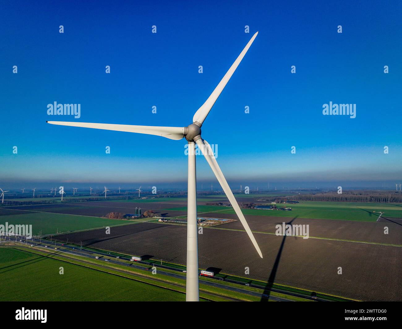 Eine majestätische Windenergieanlage steht hoch vor einem klaren blauen Himmel mit Blick auf eine grüne Landschaft Stockfoto