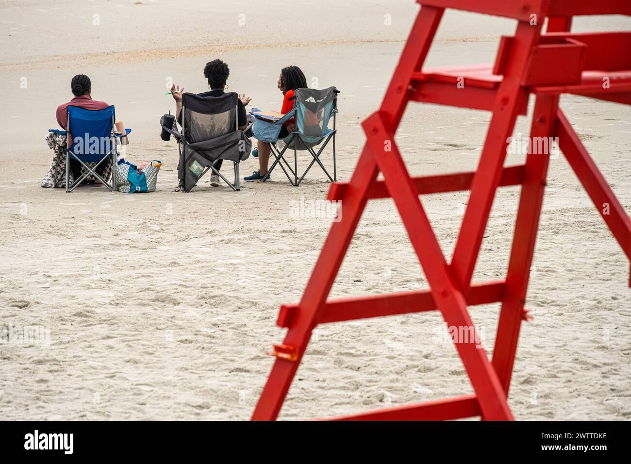 Drei Frauen, die bei Sonnenaufgang am Strand in Jacksonville Beach, Florida, eine entspannende Diskussion führen. (USA) Stockfoto