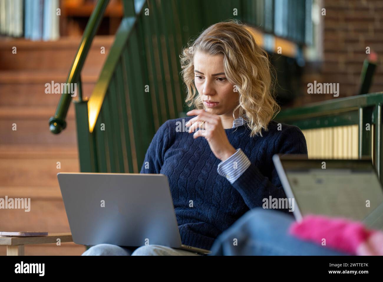Tief in Gedanken arbeitet eine Frau intensiv an ihrem Laptop in einer gemütlichen Innenumgebung. Stockfoto