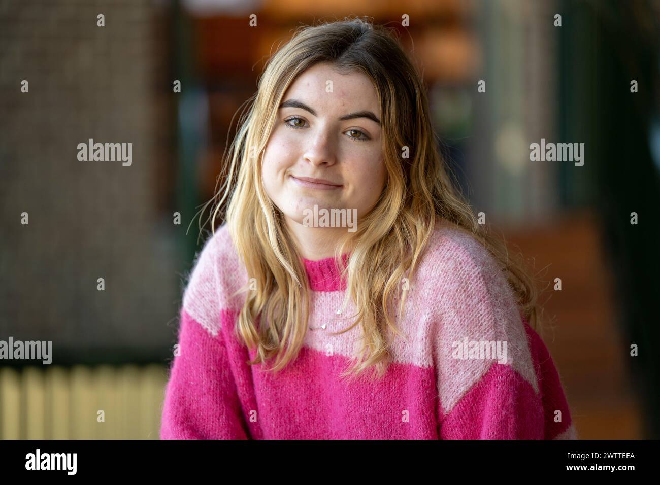 Eine junge Frau in einem rosa Pullover, die drinnen lächelt Stockfoto