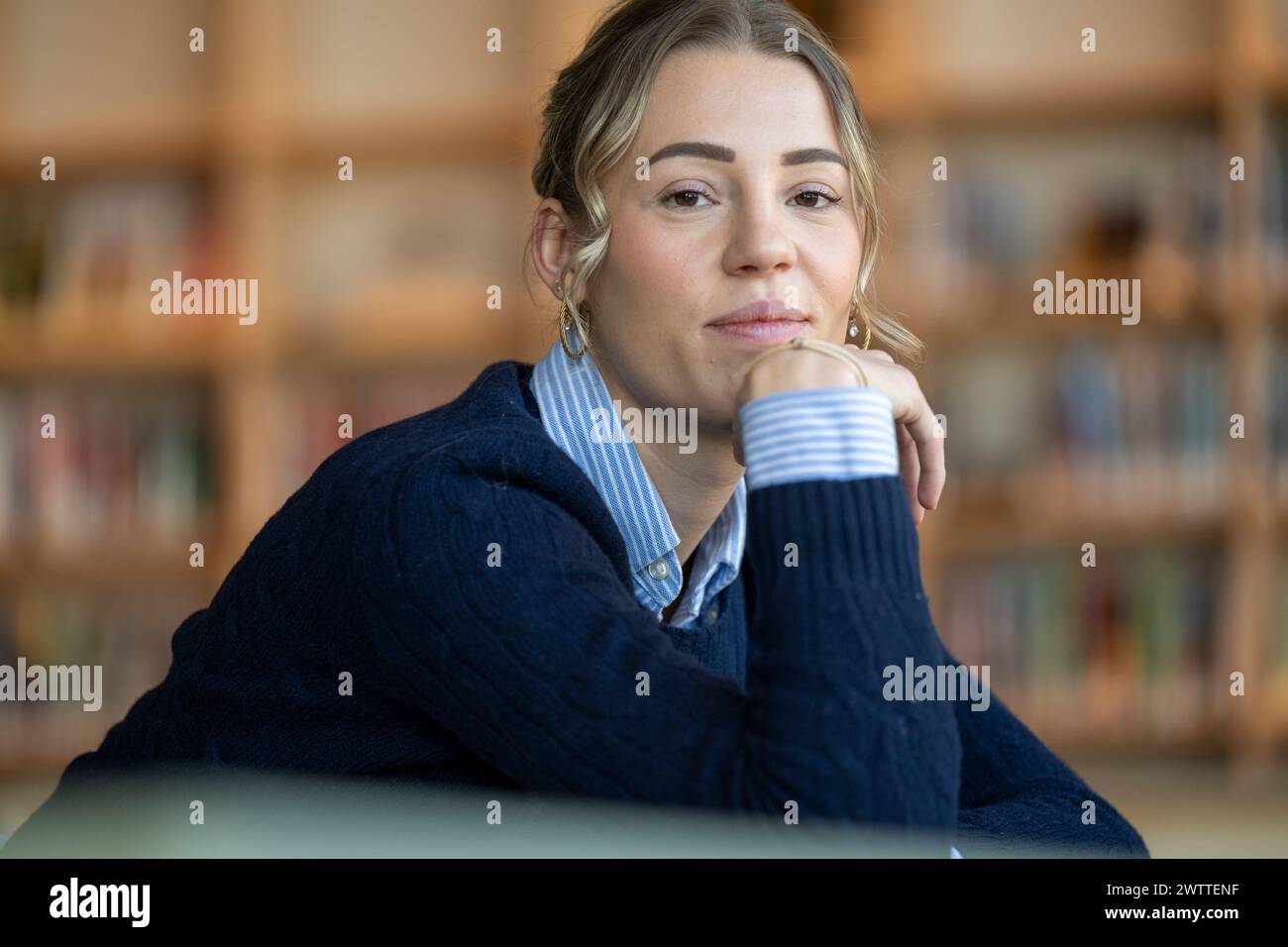 Eine besinnliche Frau, die ihr Kinn in einer Bibliothek auf der Hand hält Stockfoto