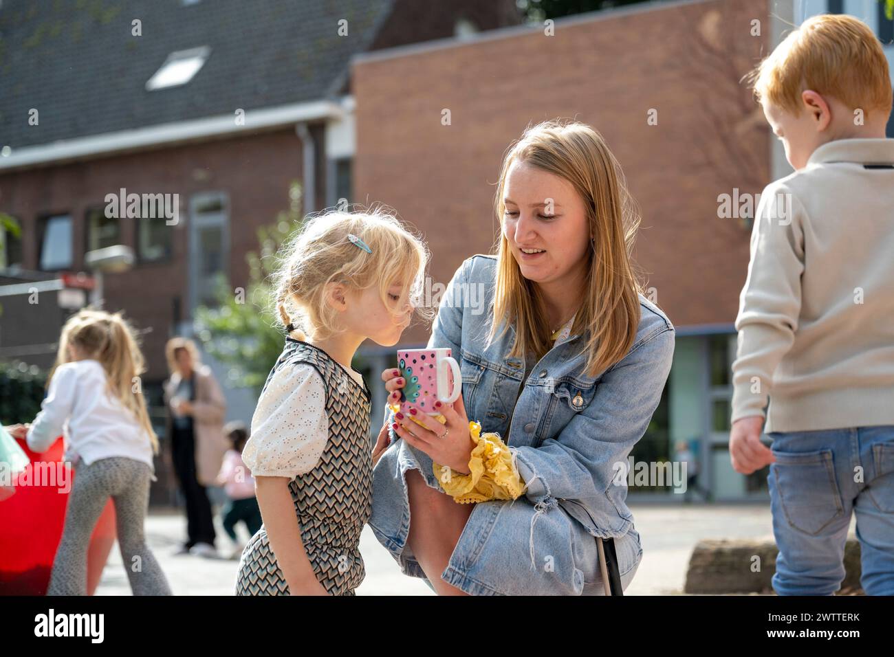 Ein fröhlicher Outdoor-Moment, in dem eine Frau etwas amüsantes auf ihrem Smartphone mit einem kleinen Mädchen teilt Stockfoto
