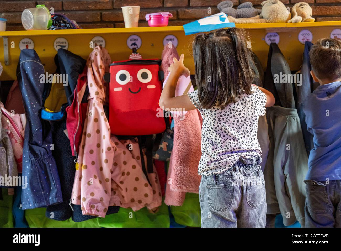Kleines Mädchen, das ihren Rucksack aus einer farbenfrohen Garderobe auswählt. Stockfoto