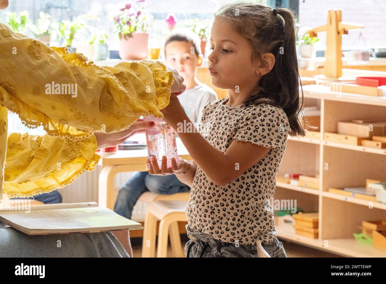 Ein junges Mädchen untersucht sorgfältig ein gelbes Kleid, das ihr in einem sonnendurchfluteten Raum übergeben wurde Stockfoto