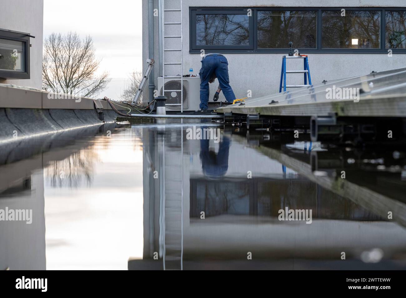 Ein Arbeiter repariert ein Dach an einem klaren Tag, der sich im stehenden Wasser spiegelt. Stockfoto