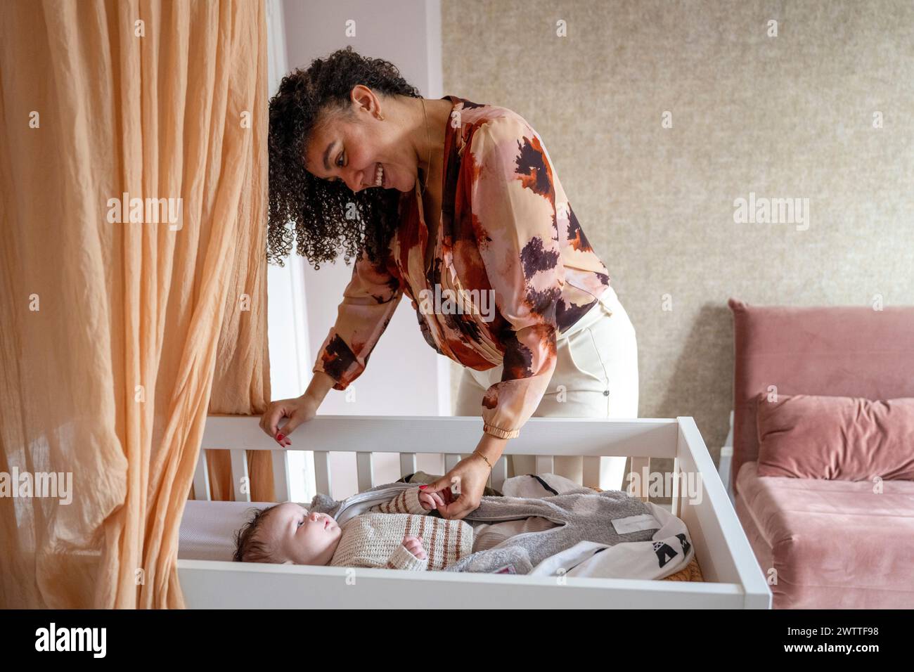 Ein zärtlicher Moment, in dem sich eine Frau über ein Kinderbett beugt, um mit einem Baby zu interagieren. Stockfoto