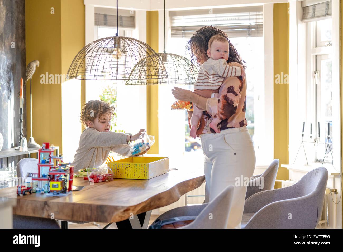 Gemütlicher Familienmoment mit Eltern, die kochen und Kindern am Küchentisch spielen. Stockfoto