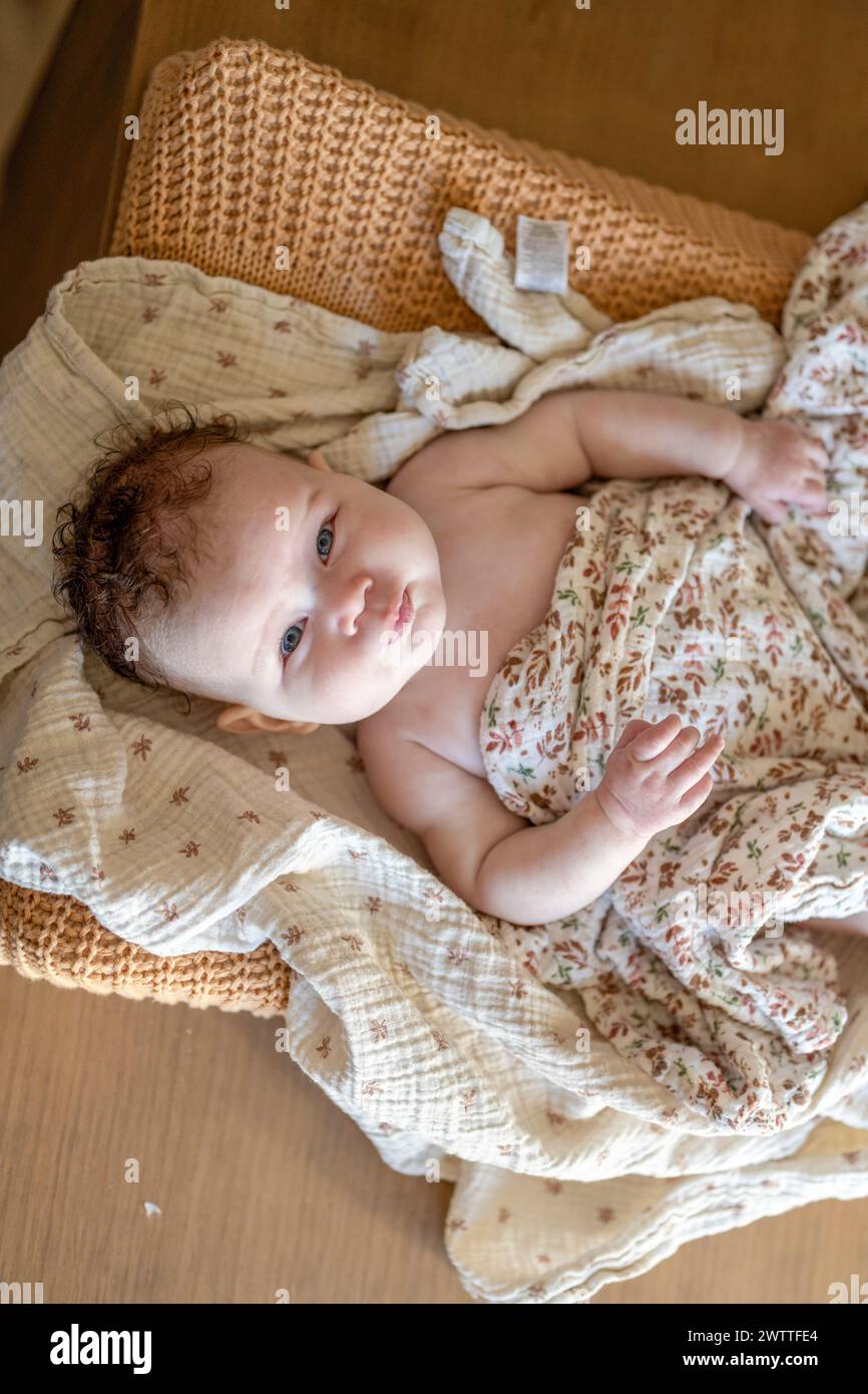 Ein neugieriges Kleinkind liegt bequem auf einer gemütlichen Decke. Stockfoto
