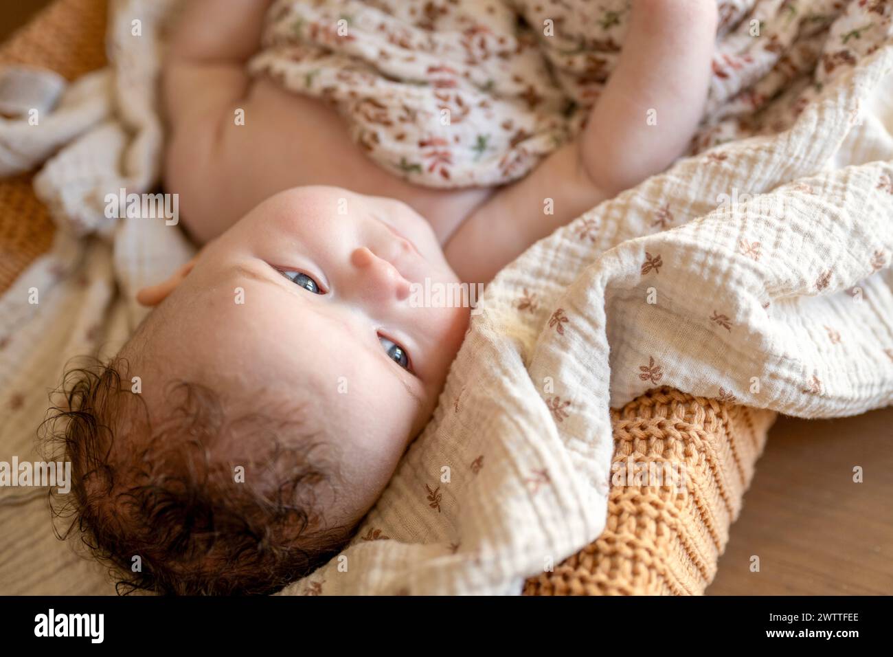 Das Baby entspannt sich auf einer gemütlichen Decke und blickt mit Interesse nach oben. Stockfoto