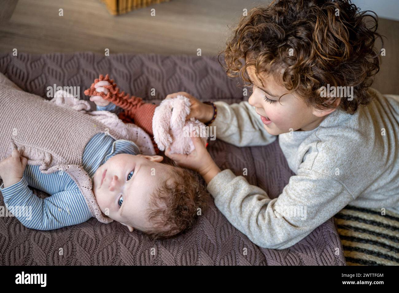 Älteres Kind interagiert zärtlich mit seinem auf einem Bett liegenden Geschwister. Stockfoto