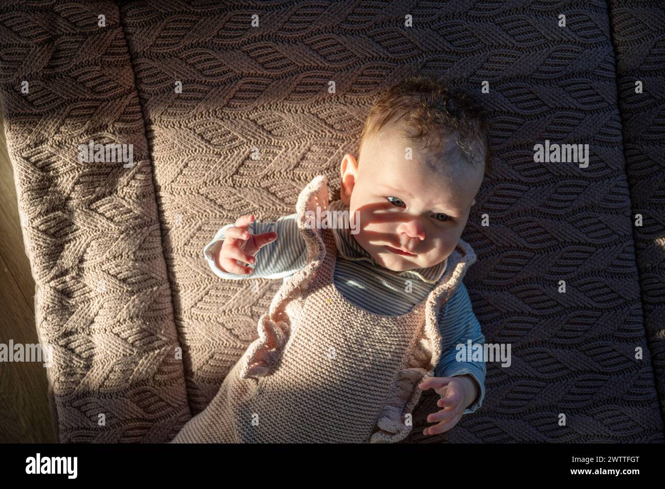 Kurioses Baby, das sich im Sonnenlicht auf einer kuscheligen Decke sonnt. Stockfoto