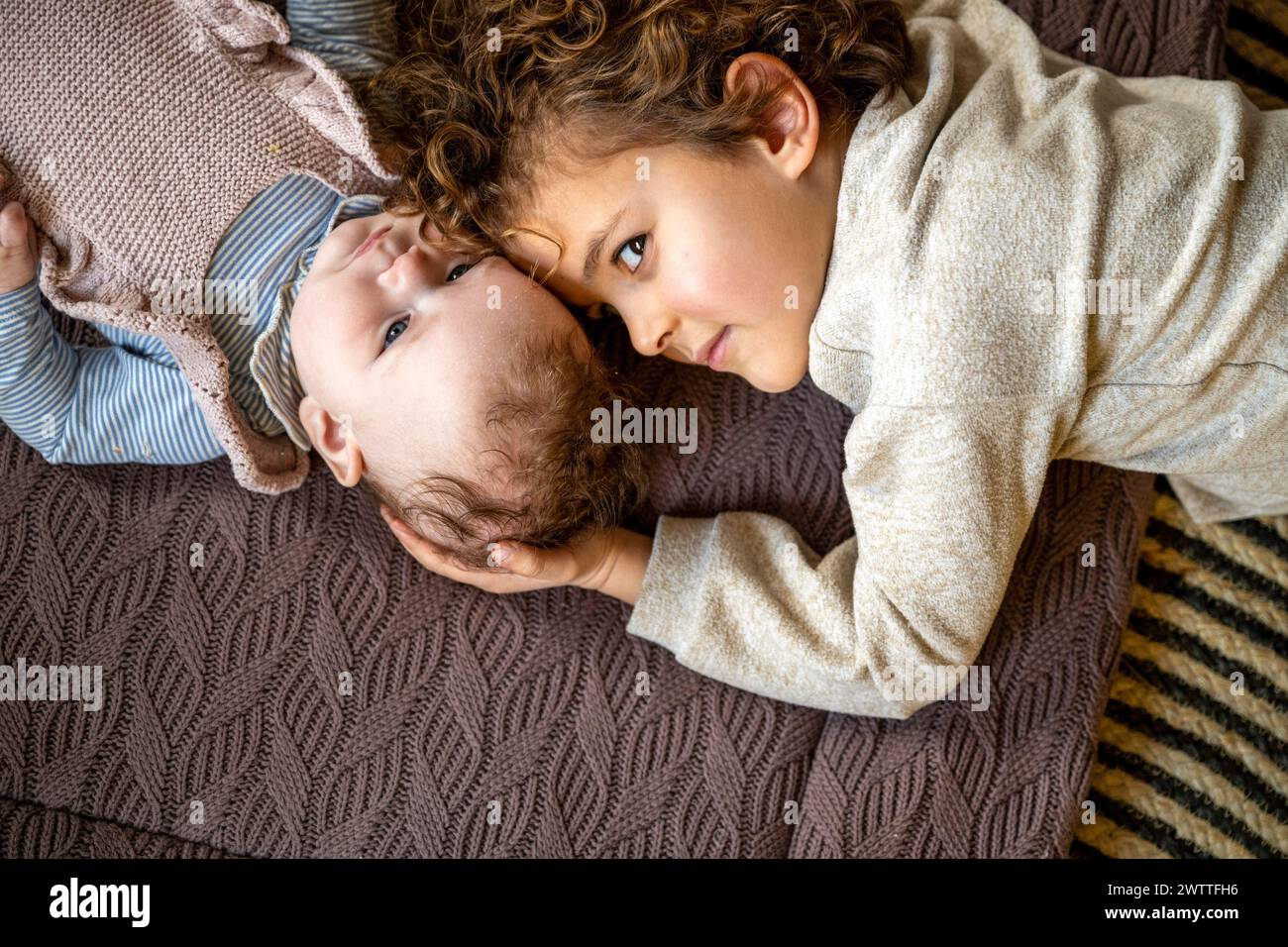 Ein zärtlicher Moment, als ein kleines Kind liebevoll ein Geschwister ansieht, das auf einer kuscheligen Strickdecke liegt. Stockfoto