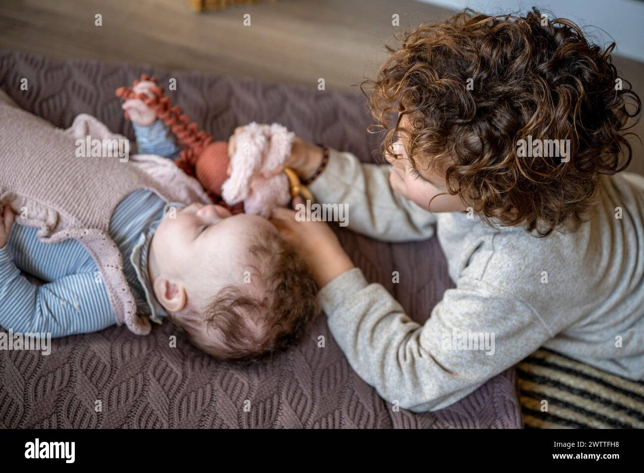 Ein älteres Geschwister interagiert zärtlich mit einem Baby, das auf einer kuscheligen Decke liegt. Stockfoto