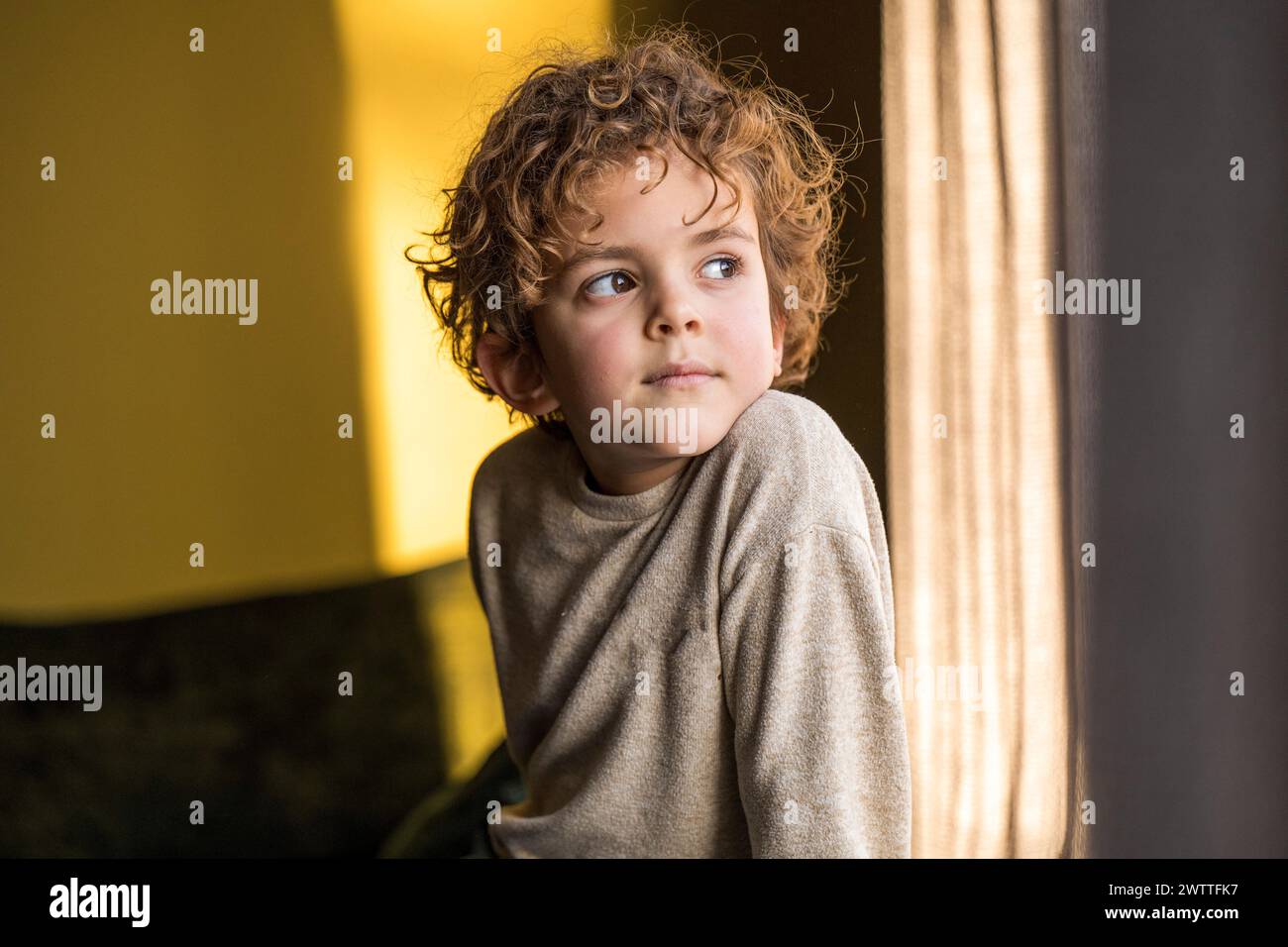 Ein kleines Kind, das aus einem sonnendurchfluteten Fenster blickt Stockfoto