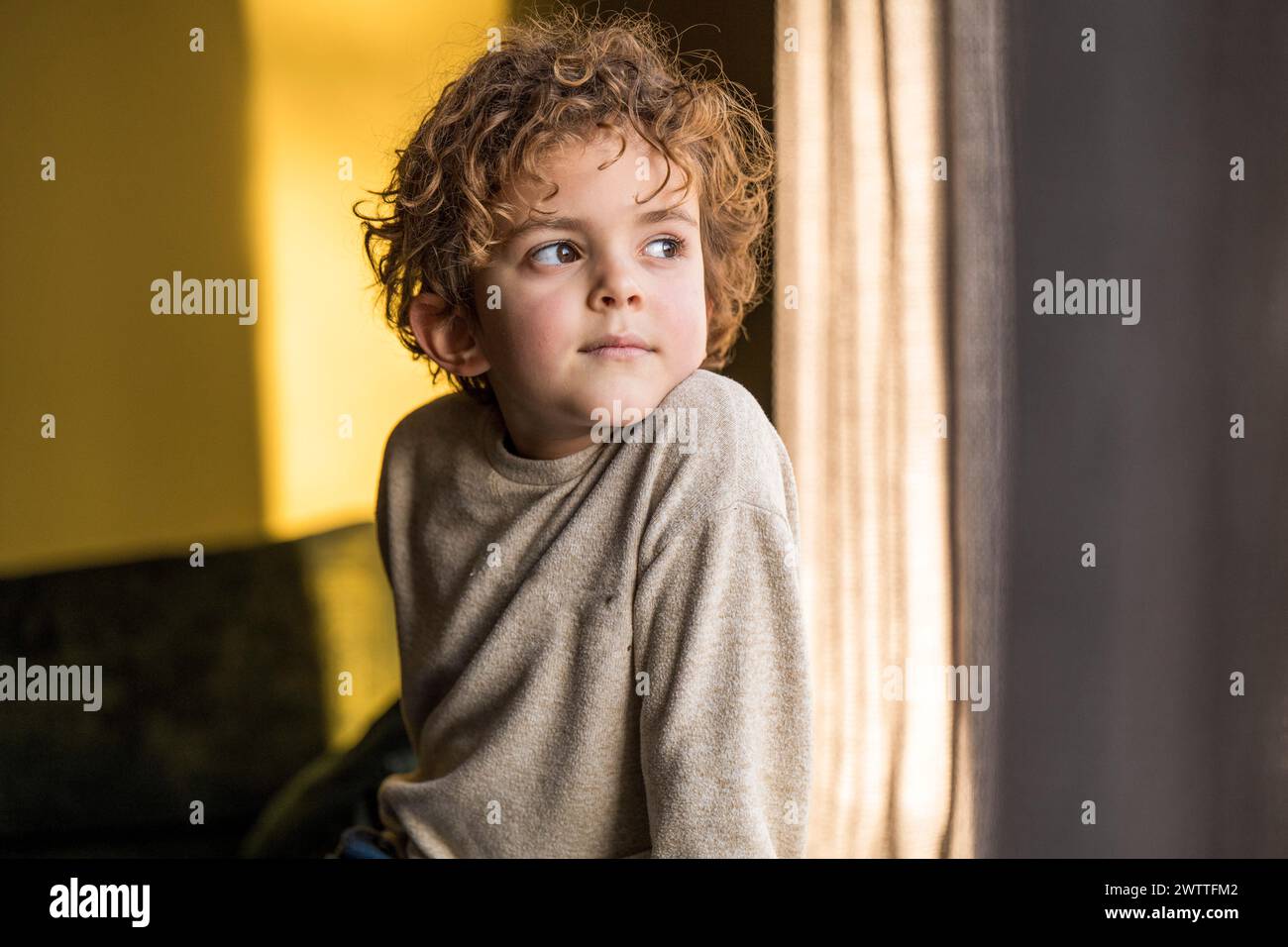 Neugieriges Kind, das mit einem nachdenklichen Ausdruck aus dem Fenster blickt. Stockfoto