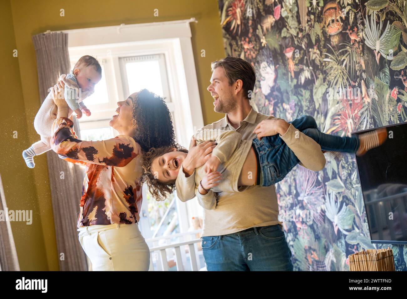 Familienspaß, wenn Eltern ihre Kinder im Haus spielerisch hochheben Stockfoto