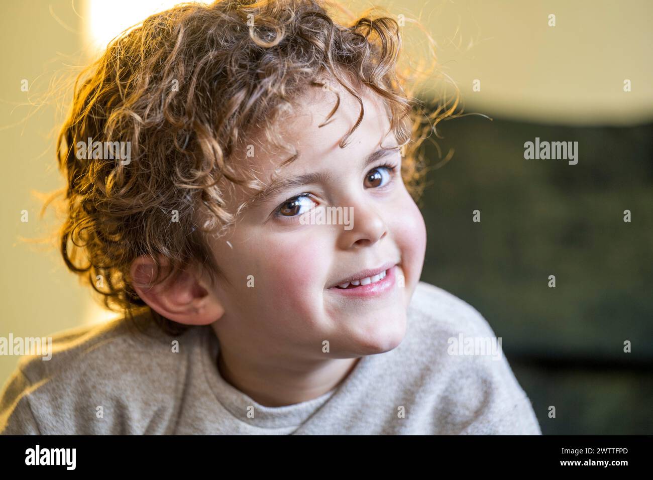 Lächelndes Kind mit lockigem Haar, das einen verspielten Moment genießt Stockfoto
