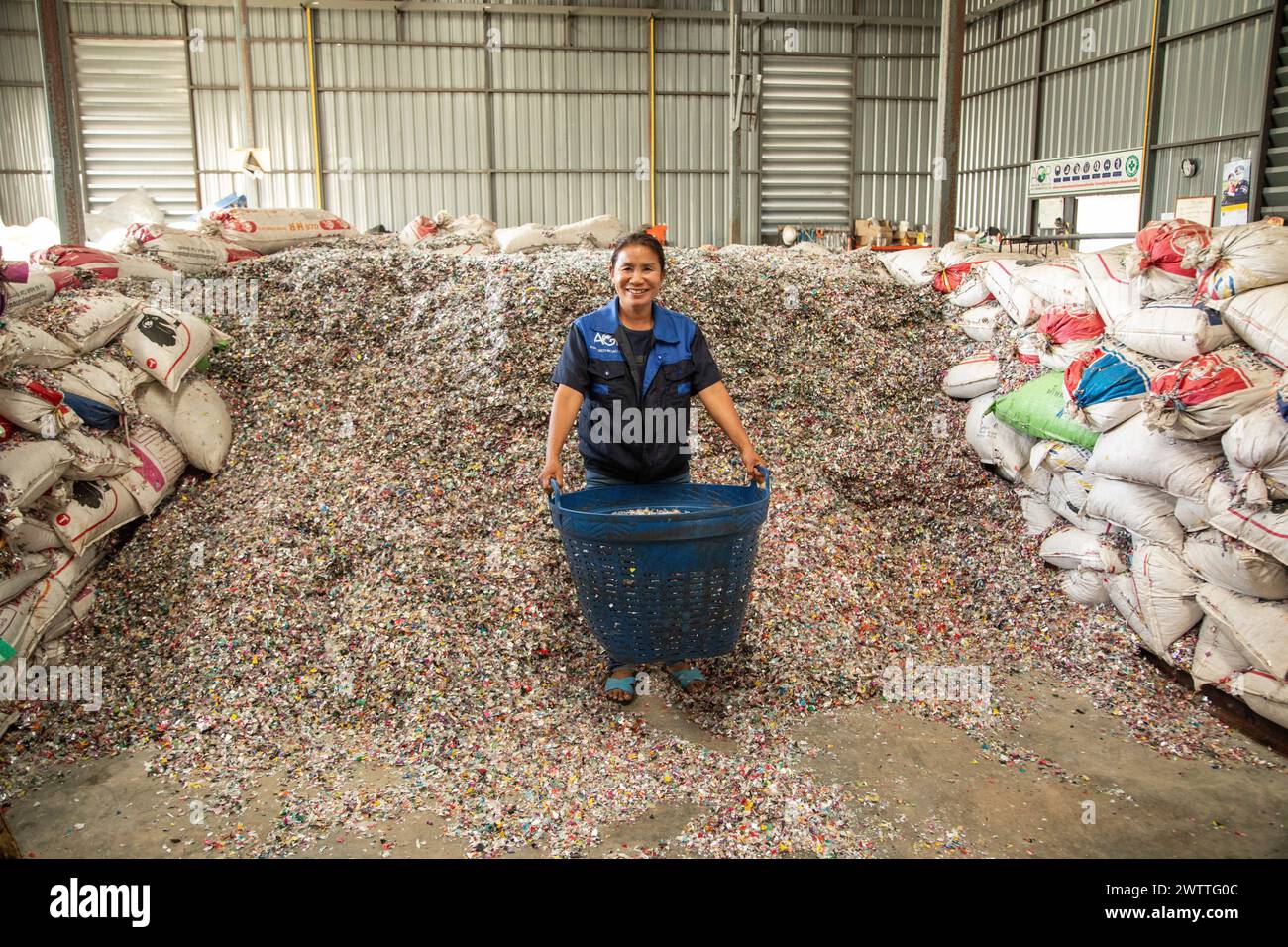 Arbeiter lächelt inmitten eines Berges von Plastikflaschenverschlüssen zum Recycling, Plastikrecyclingfabrik, Thailand Stockfoto