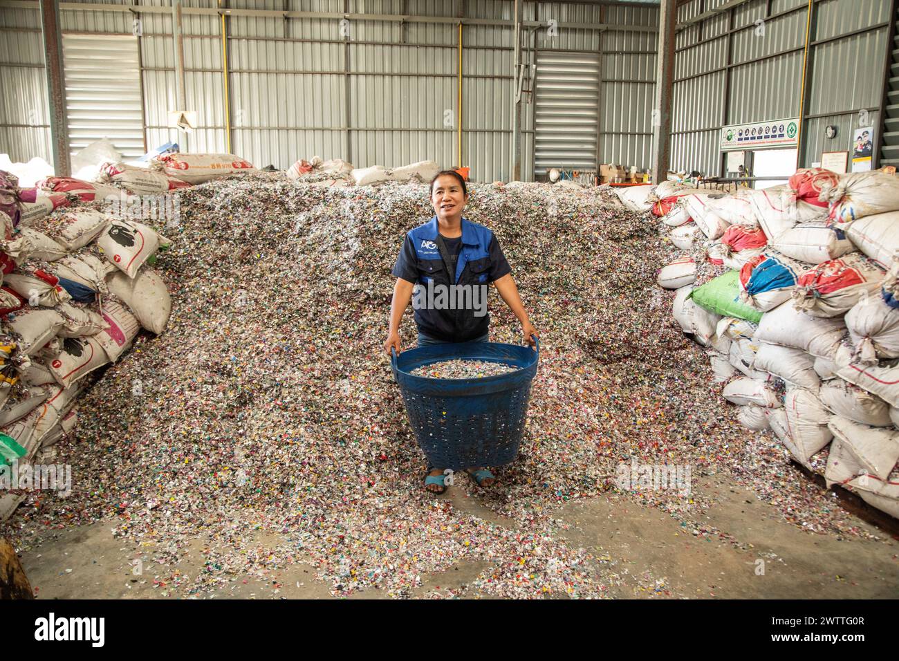 Arbeiter lächelt inmitten eines Berges von Plastikflaschenverschlüssen zum Recycling, Plastikrecyclingfabrik, Thailand Stockfoto