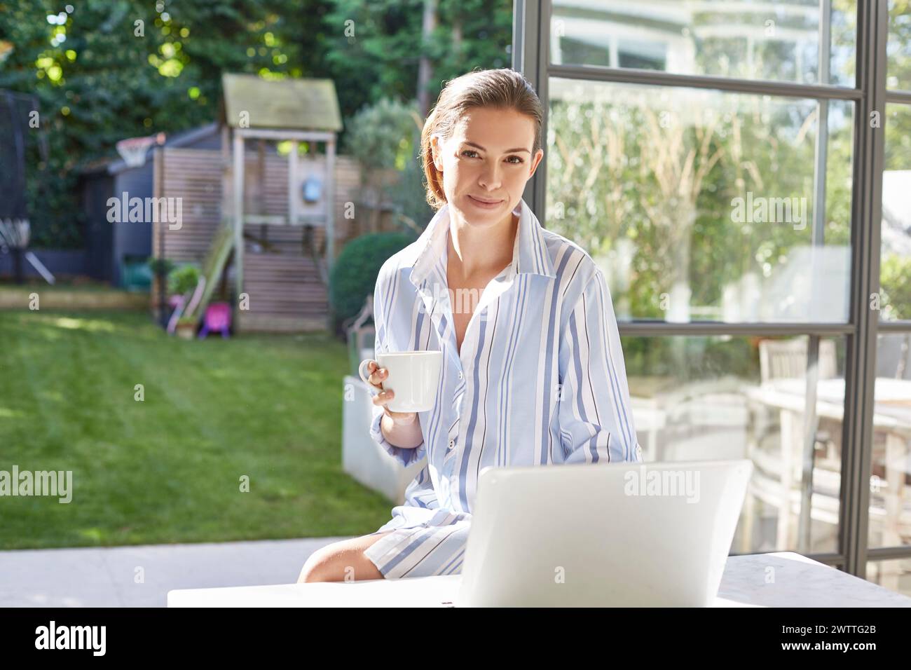 Frau mit Kaffee und Laptop in einem sonnigen Garten Stockfoto