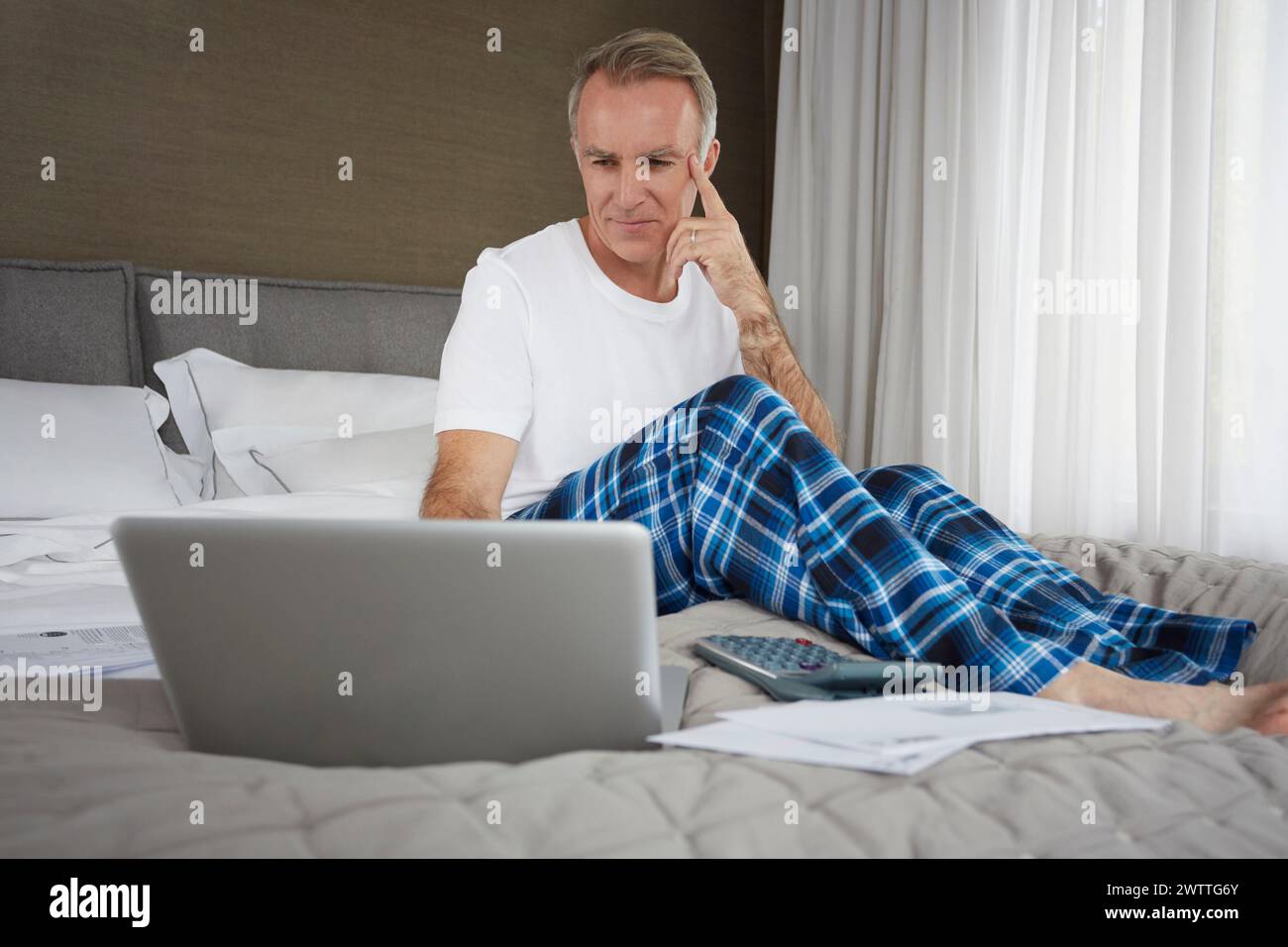 Mann mit Laptop, der auf einem Bett sitzt Stockfoto