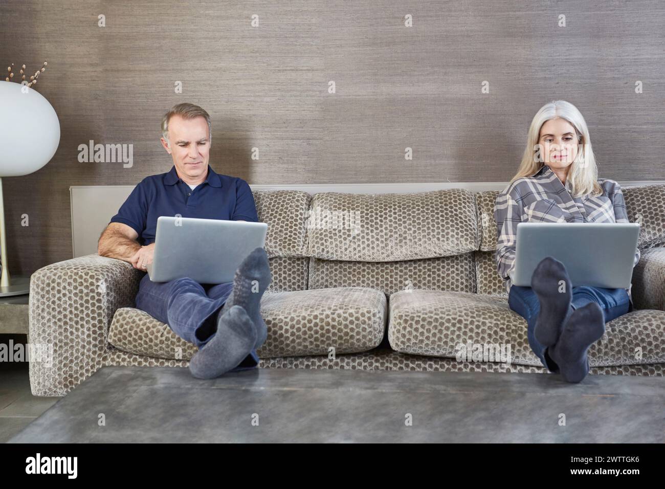 Zwei Personen arbeiten auf Laptops, während sie auf einer Couch sitzen. Stockfoto