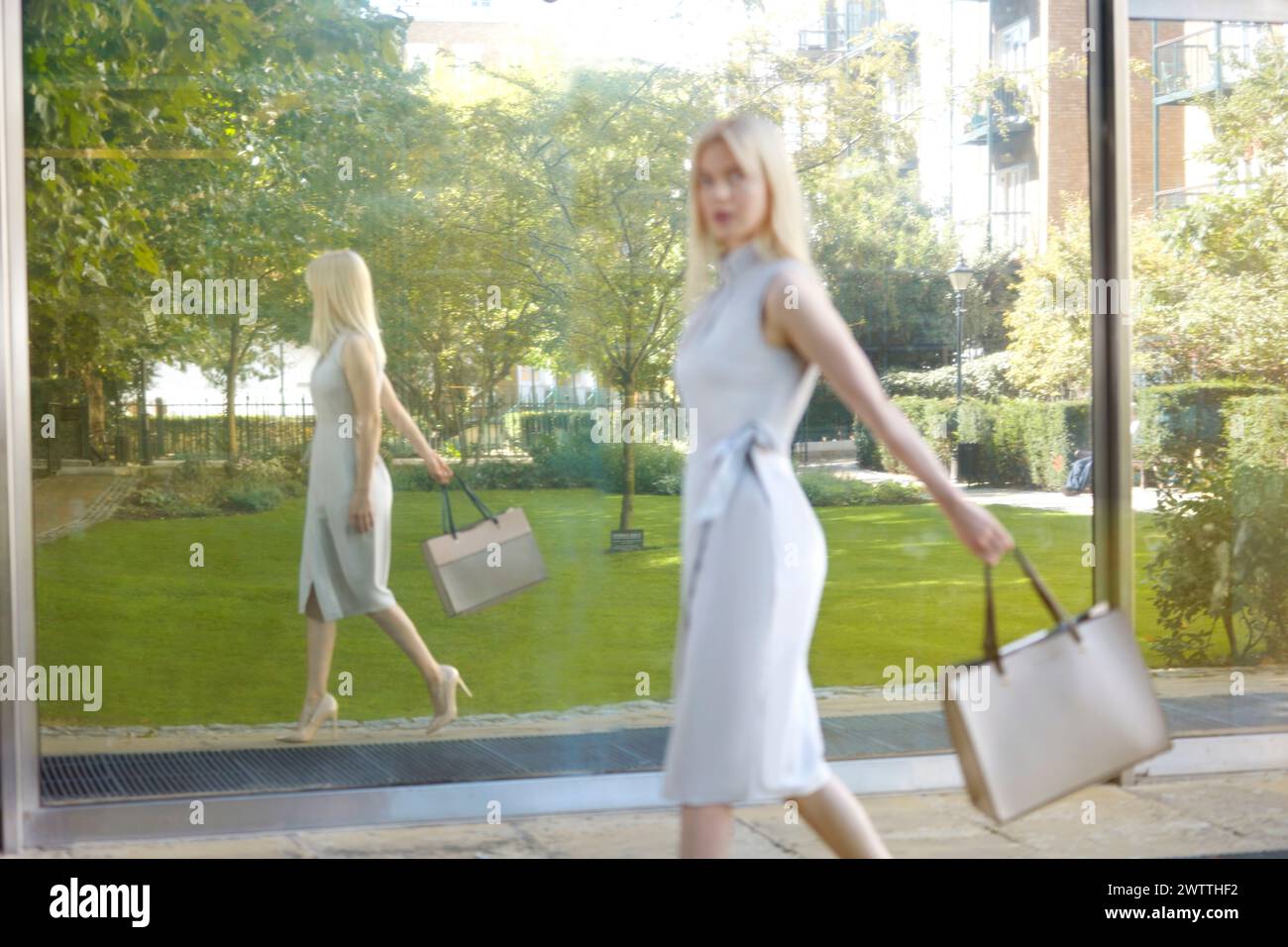 Frau, die an einer reflektierenden Glasoberfläche vorbeigeht Stockfoto