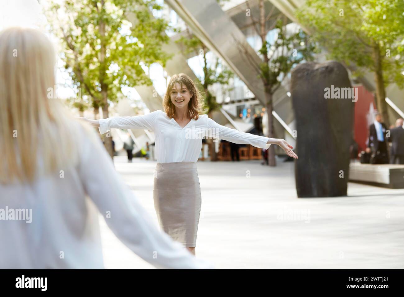 Frau mit ausgebreiteten Armen lächelt zu einer anderen Stockfoto