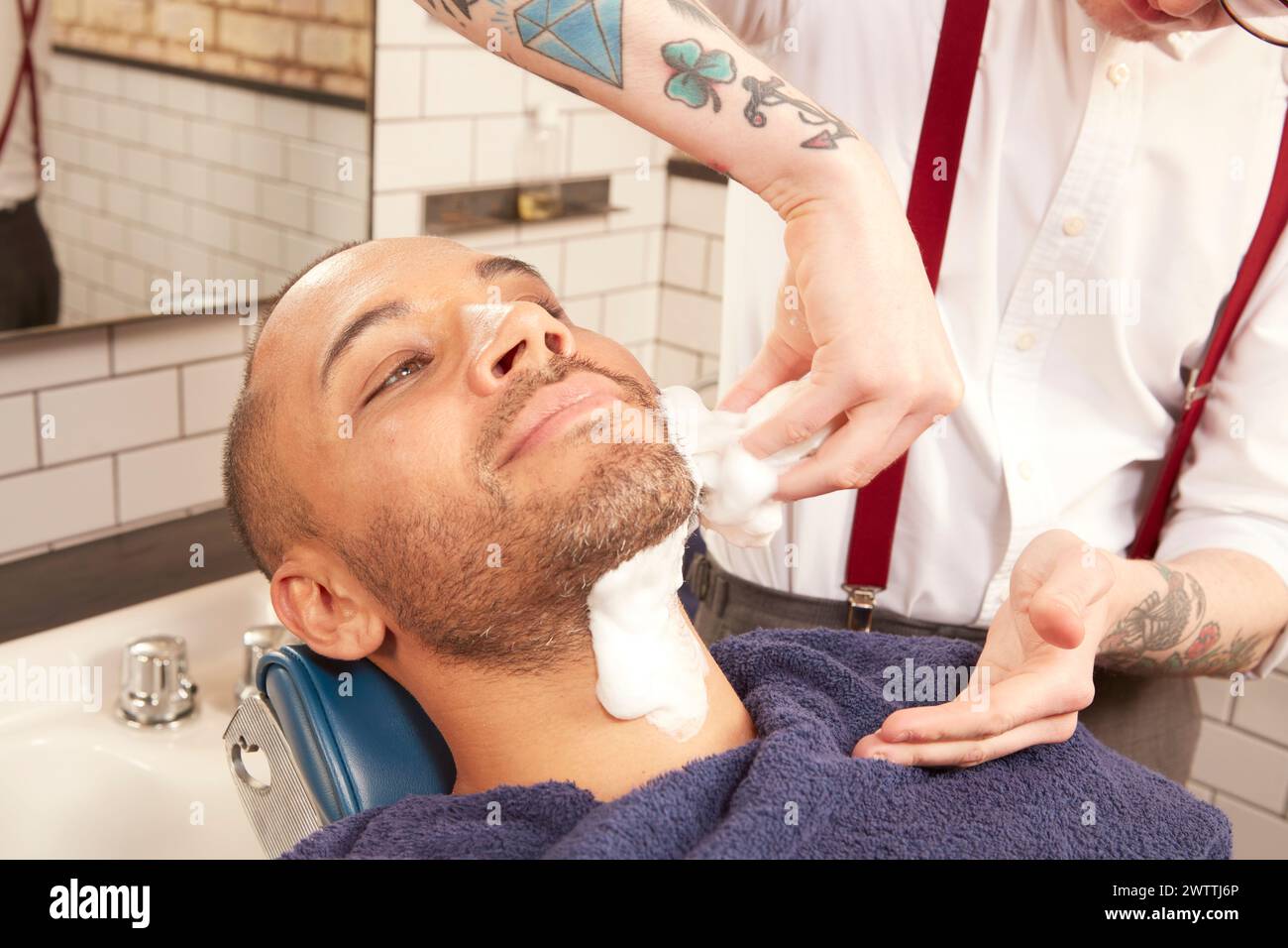 Friseur, der Rasiercreme auf das Gesicht des Kunden aufträgt Stockfoto