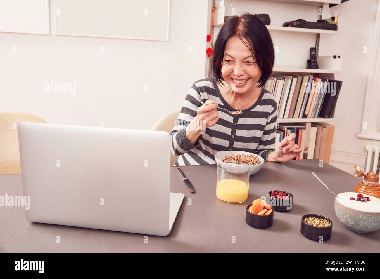 Frau frühstückt, während sie an einem Laptop arbeitet. Stockfoto