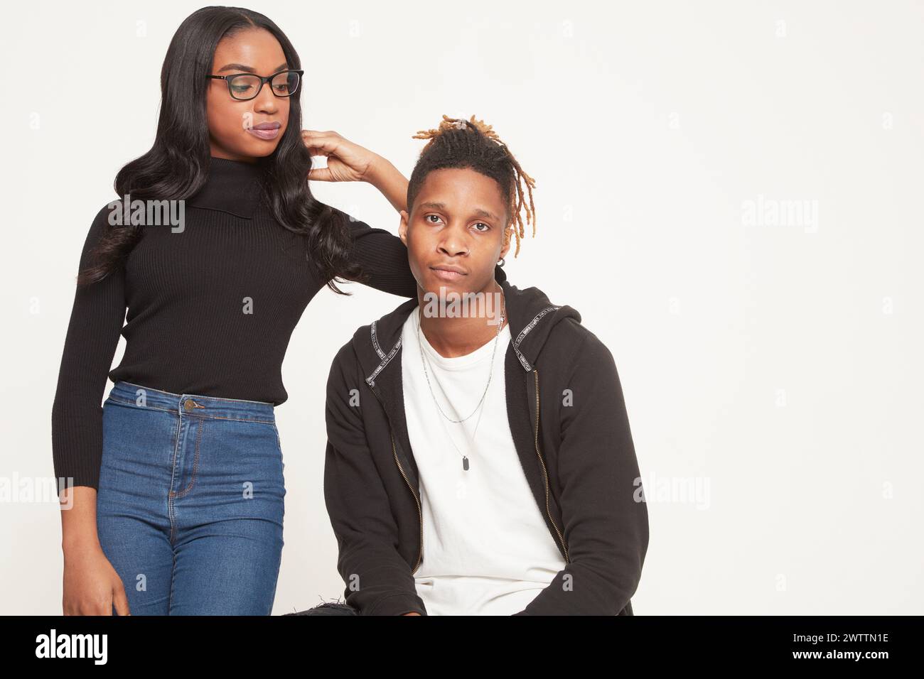 Frau, die neben einem sitzenden Mann vor weißem Hintergrund steht. Stockfoto