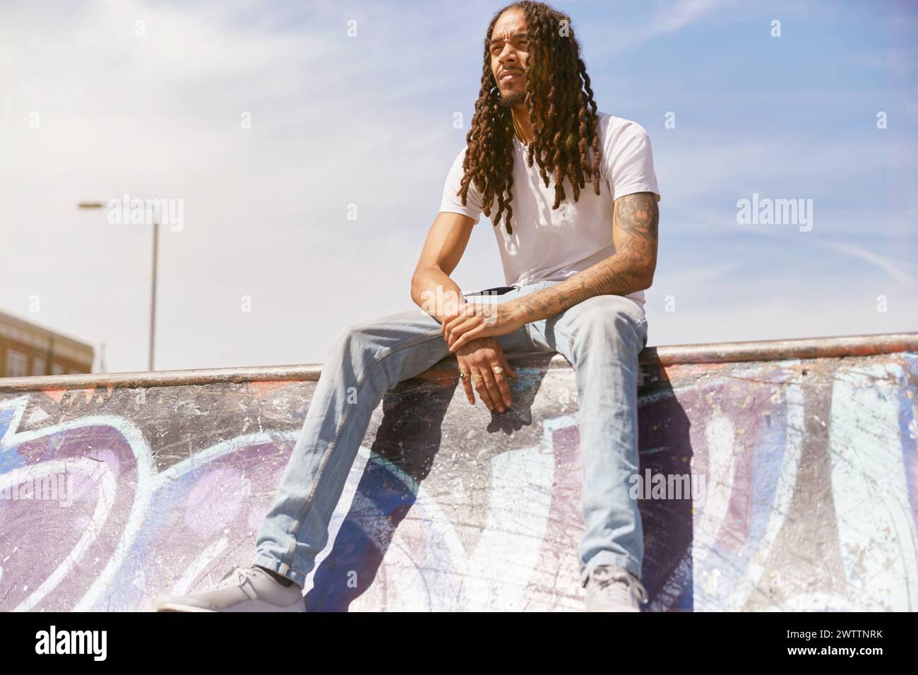 Mann, der unter der Sonne auf einer Graffiti-Wand sitzt. Stockfoto
