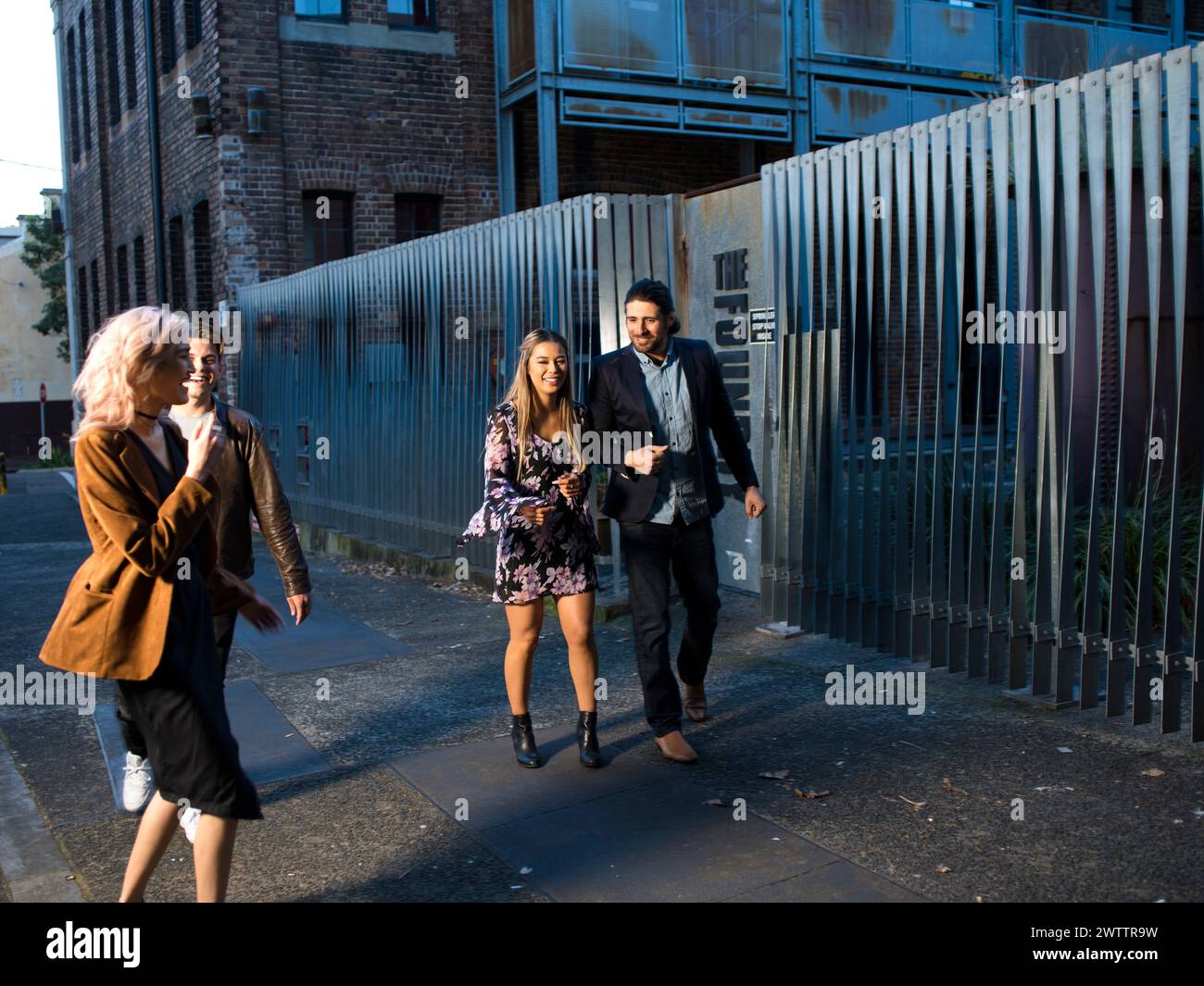 Drei Personen, die an einem Metallzaun in einer städtischen Umgebung vorbeilaufen Stockfoto