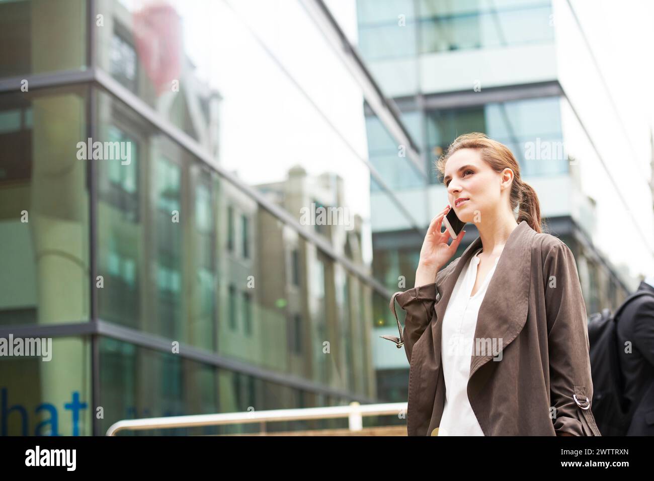Frau, die am Telefon vor Glasgebäuden spricht. Stockfoto