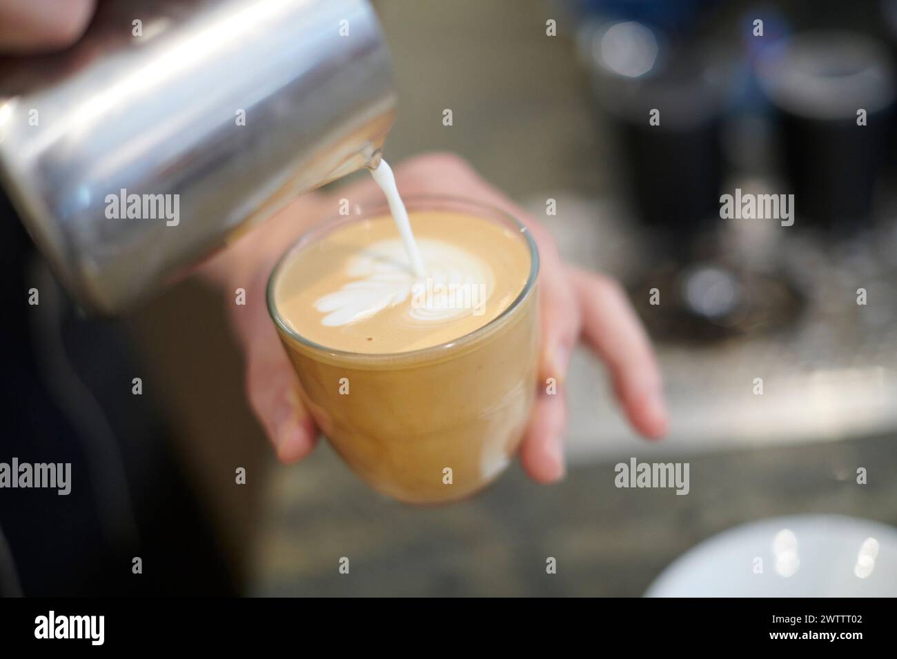 Der Barista gießt Milch in den Kaffee und kreiert so Latte Art Stockfoto