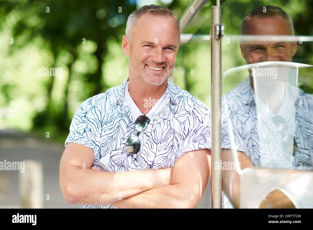 Ein lächelnder Mann in einem gemusterten Hemd, der sich auf eine Glasscheibe stützt. Stockfoto