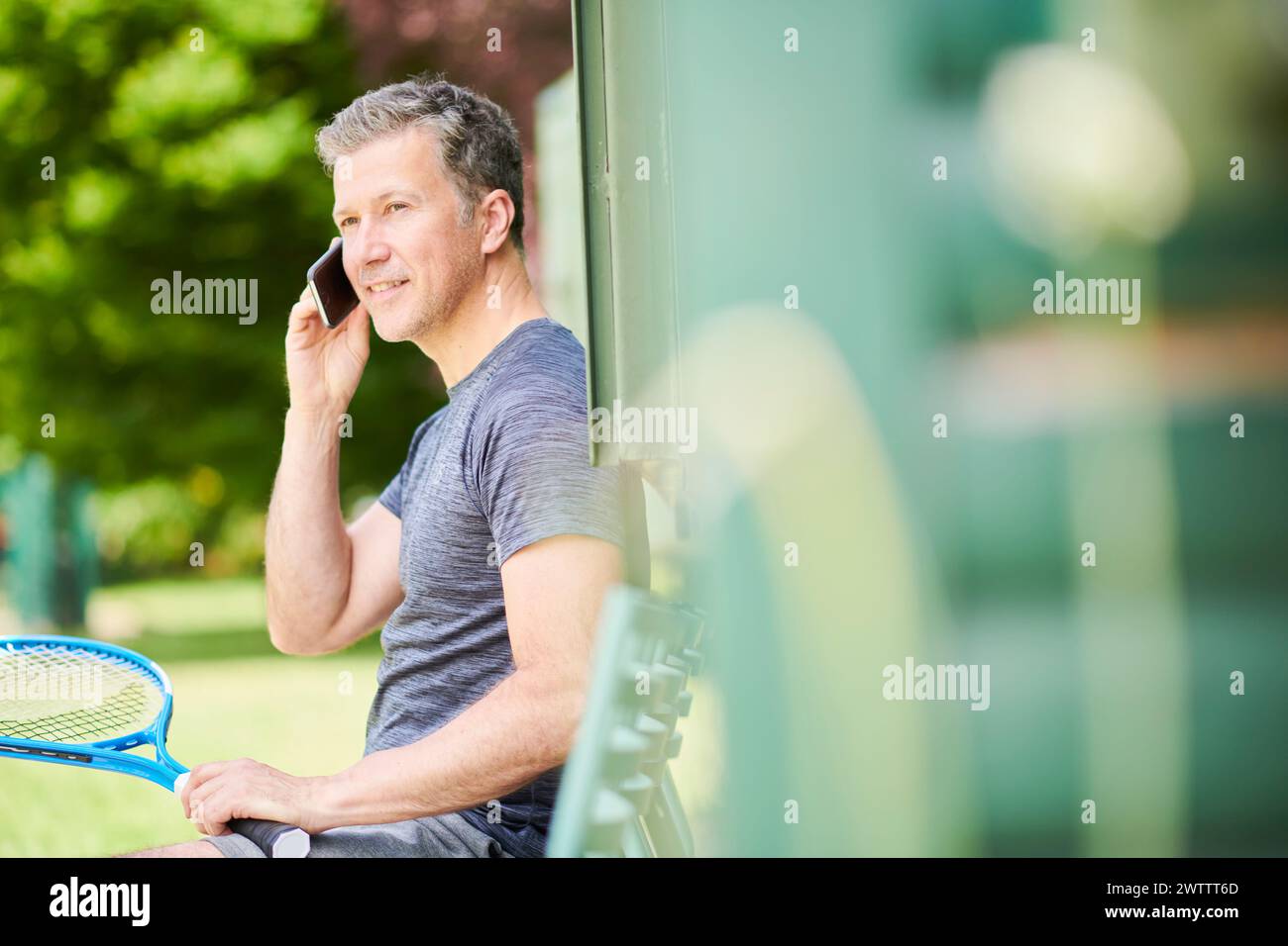 Mann mit einem Tennisschläger, der draußen telefoniert Stockfoto