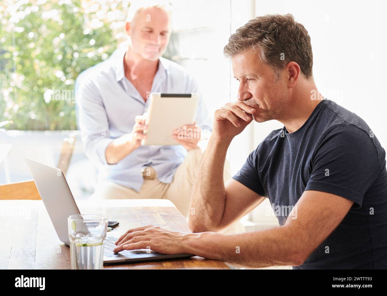 Zwei Männer, die an einem Tisch mit Laptop und Tablet arbeiten. Stockfoto