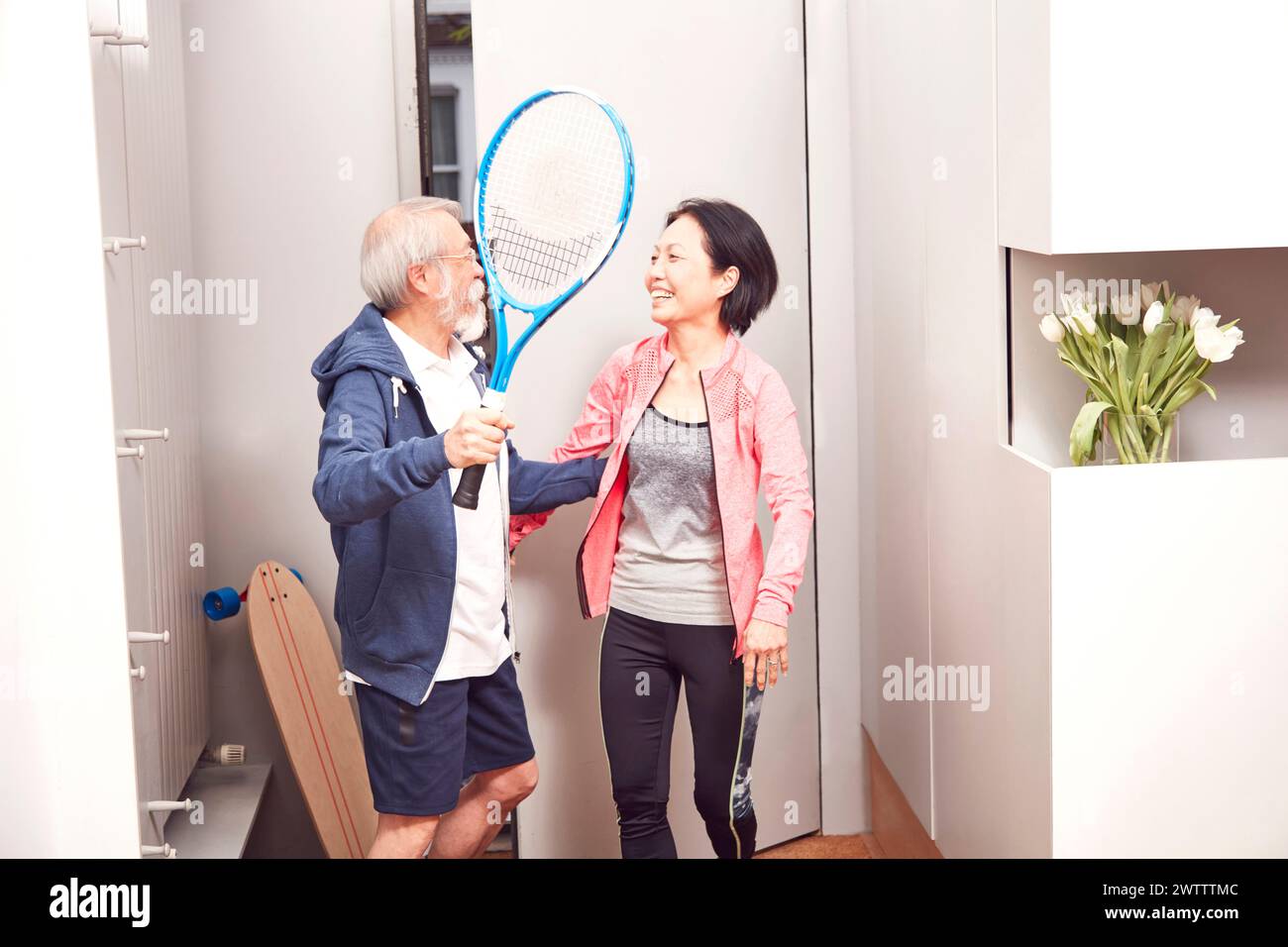 Seniorenpaar mit Tennisschlägern, die drinnen lachen Stockfoto