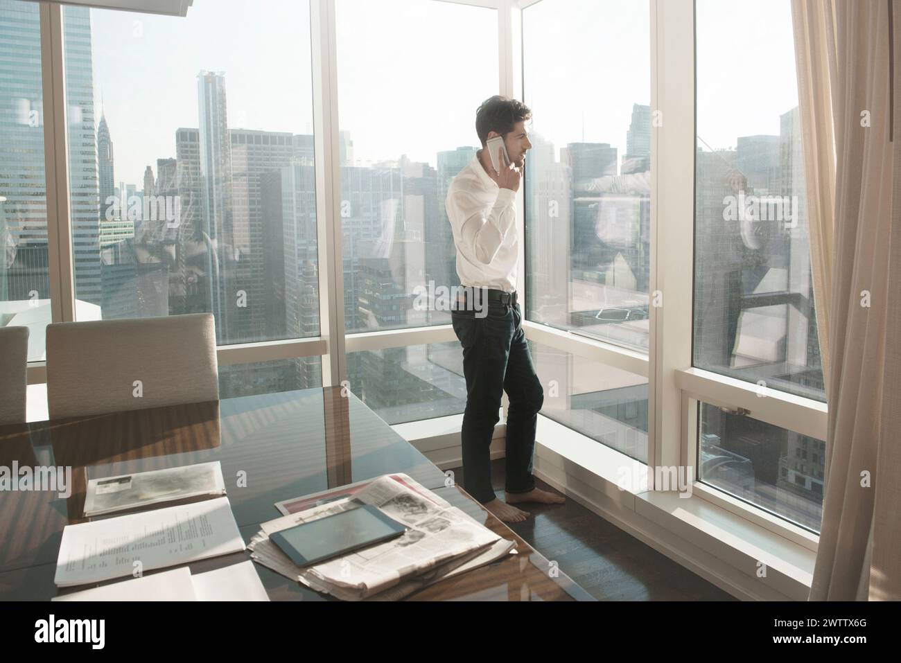 Mann am Telefon am Fenster mit Blick auf die Stadt Stockfoto