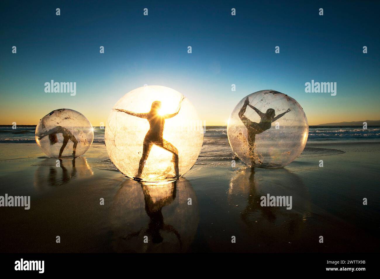 Silhouettenfiguren in transparenten Kugeln am Strand bei Sonnenuntergang Stockfoto