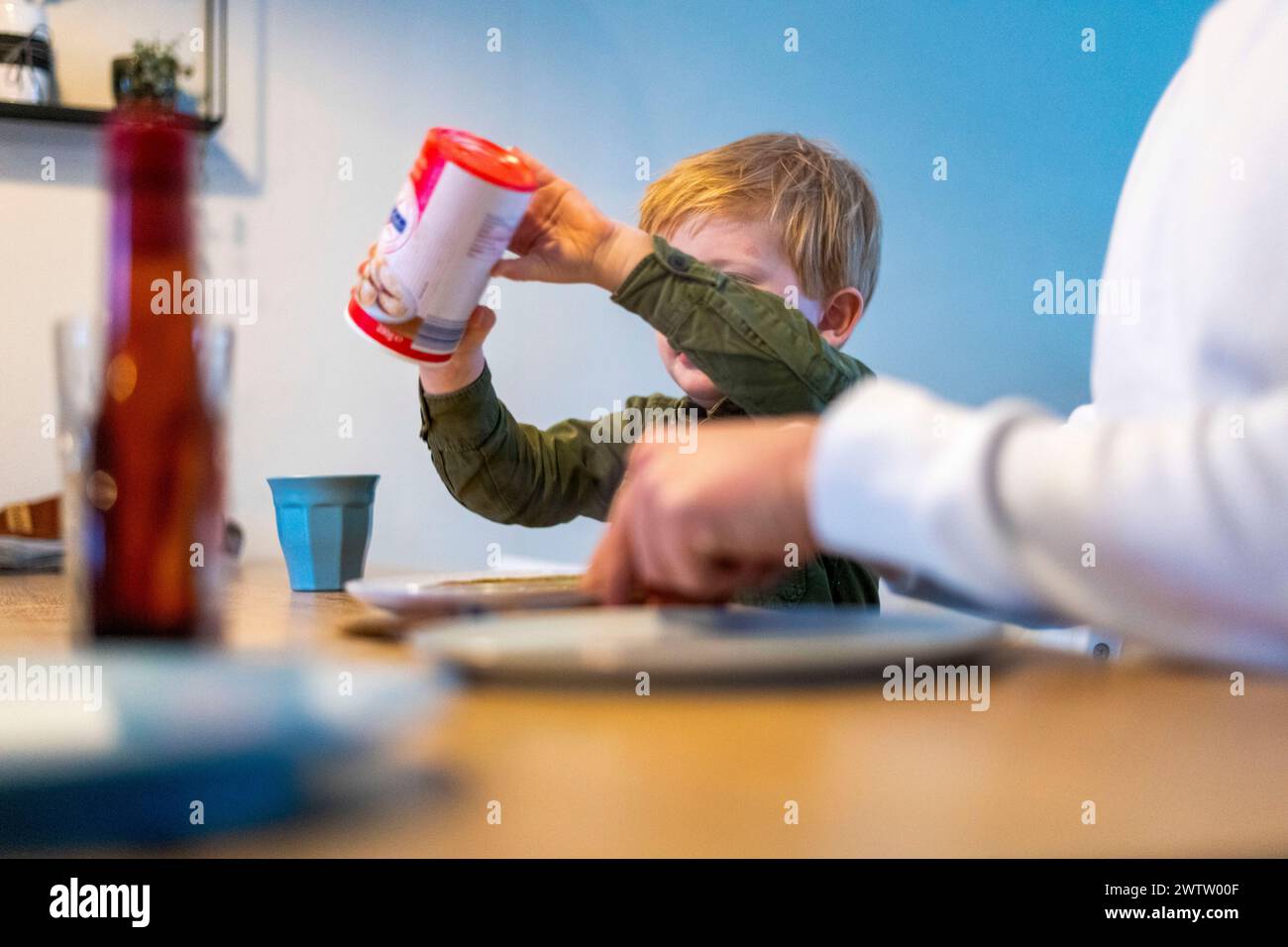 Ein neugieriges Kind, das versucht, Ketchup während eines Familienessens auf den Teller zu gießen. Stockfoto
