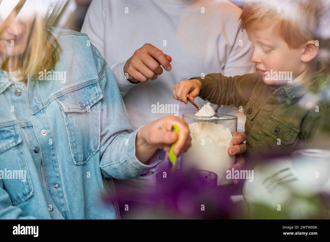 Familienmoment als kleines Kind lernt, mit Hilfe von Erwachsenen Mehl zum Backen zu schöpfen. Stockfoto