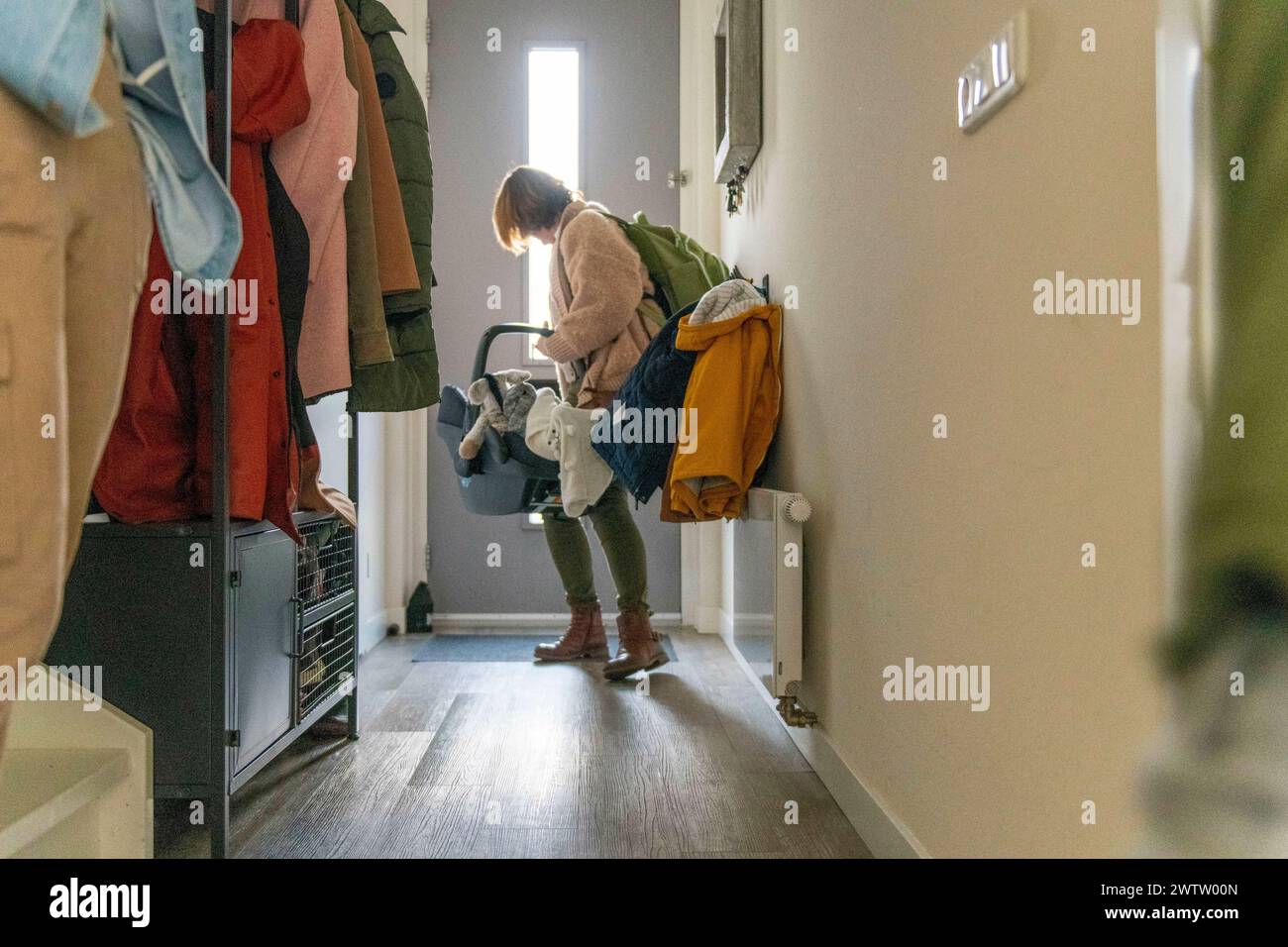 Eine Person sortiert die Wäsche in einem hellen, gemütlichen Flur, gefüllt mit Mänteln, die an Haken hängen. Stockfoto