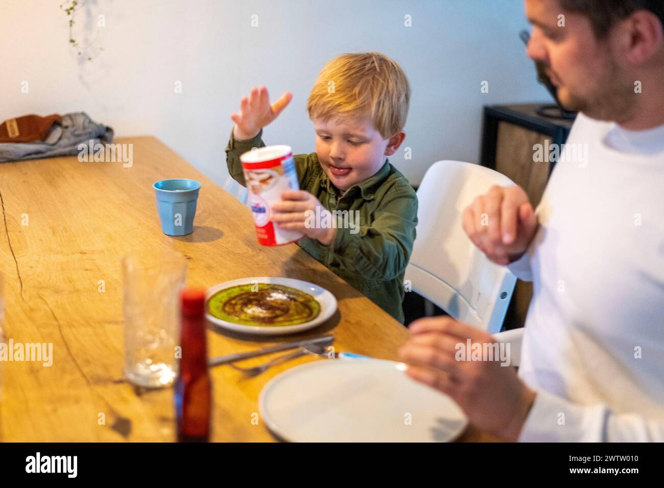 Das kleine Kind lernt aufgeregt, einen Salzstreuer während der Familienmahlzeit zu benutzen. Stockfoto