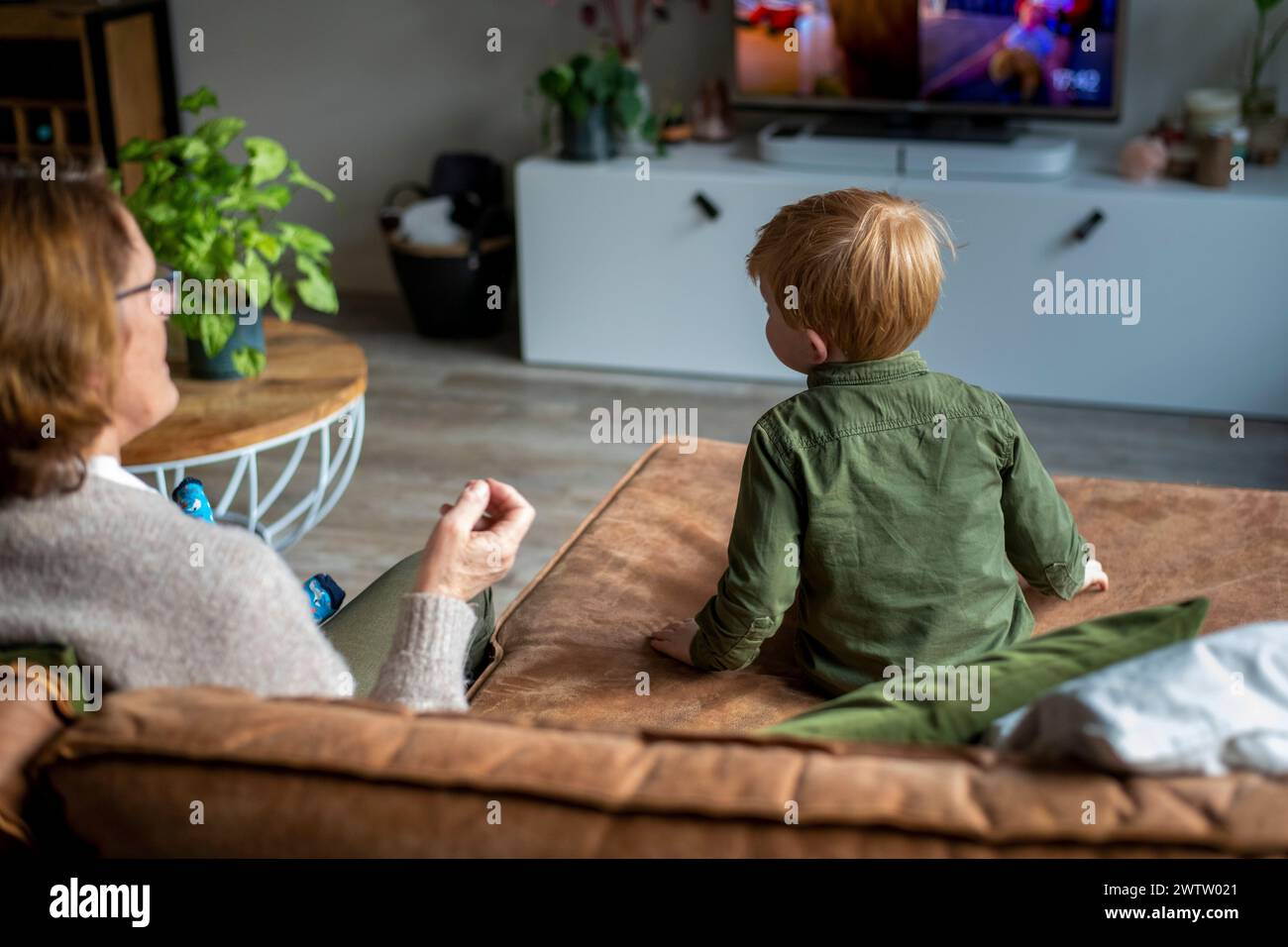 Großmutter und Enkel genießen die gemeinsame Zeit zu Hause, während sich das Kind auf den Fernseher konzentriert Stockfoto