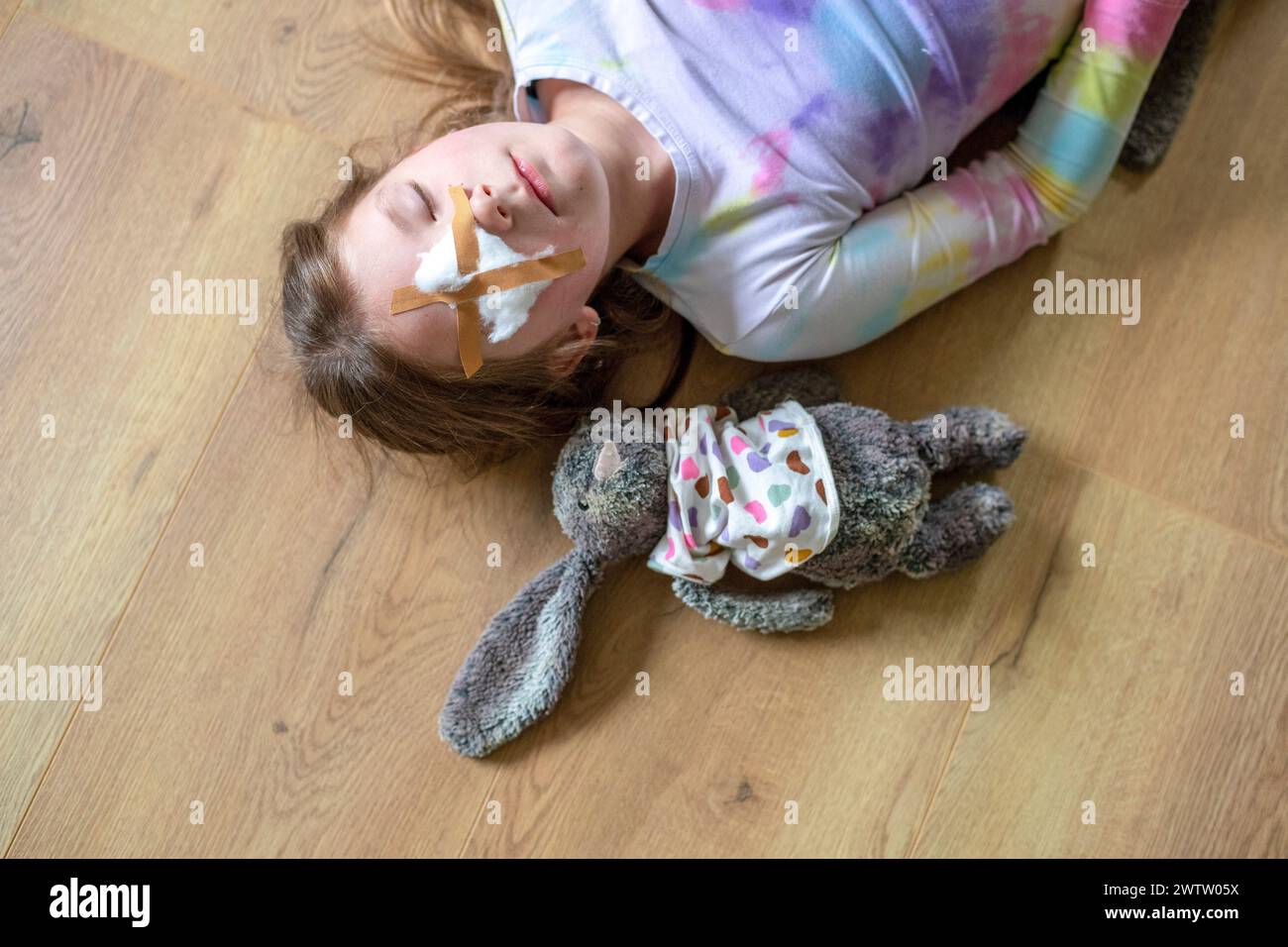 Ein junges Mädchen liegt auf dem Boden mit einem Plüschhasen und einem Blatt im Gesicht und genießt einen ruhigen Moment. Stockfoto