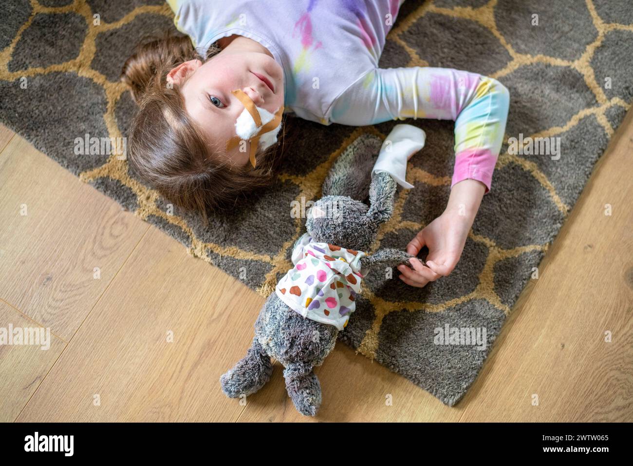 Ein junges Mädchen liegt auf dem Boden mit ihrem angefüllten Häschen, beide tragen Gesichtsmasken. Stockfoto